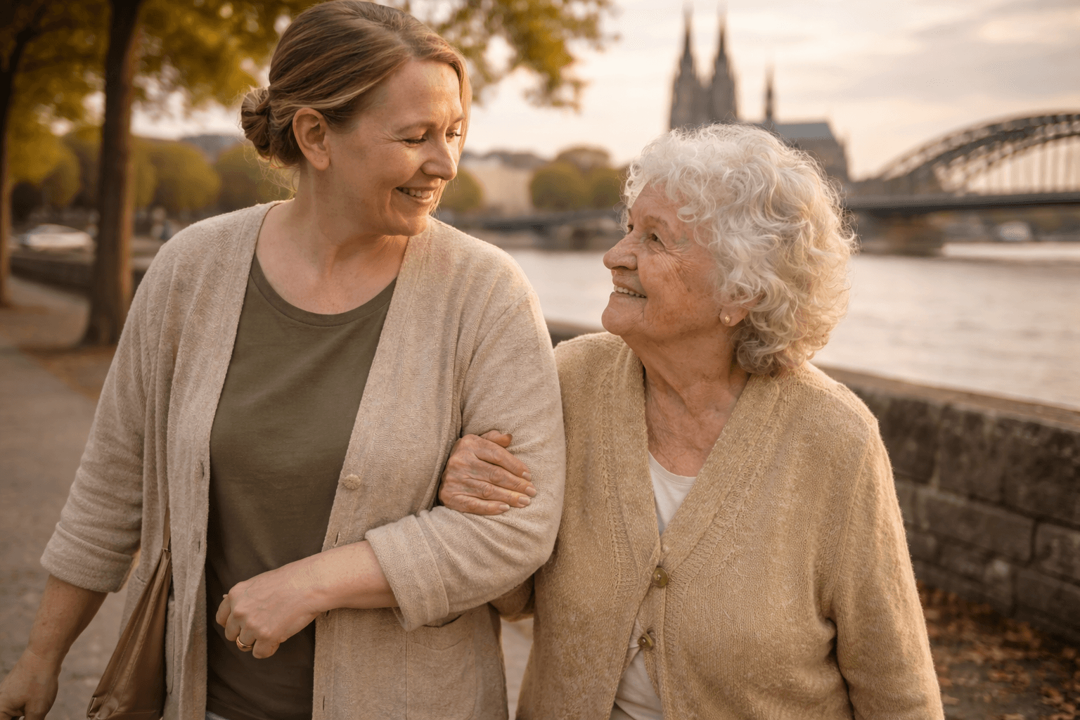 Alltagsbegleiterin und Seniorin beim Spaziergang am Rhein mit dem Kölner Dom im Hintergrund